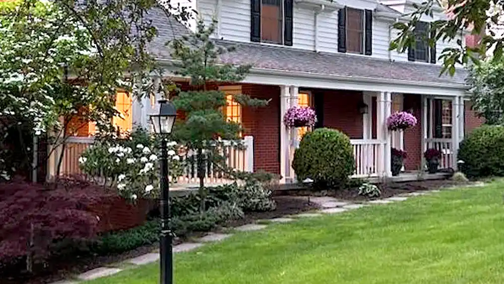 THE Landscape Pro - Paula Testimonial Front yard of red brick house with hanging annuals and manicured shrubs